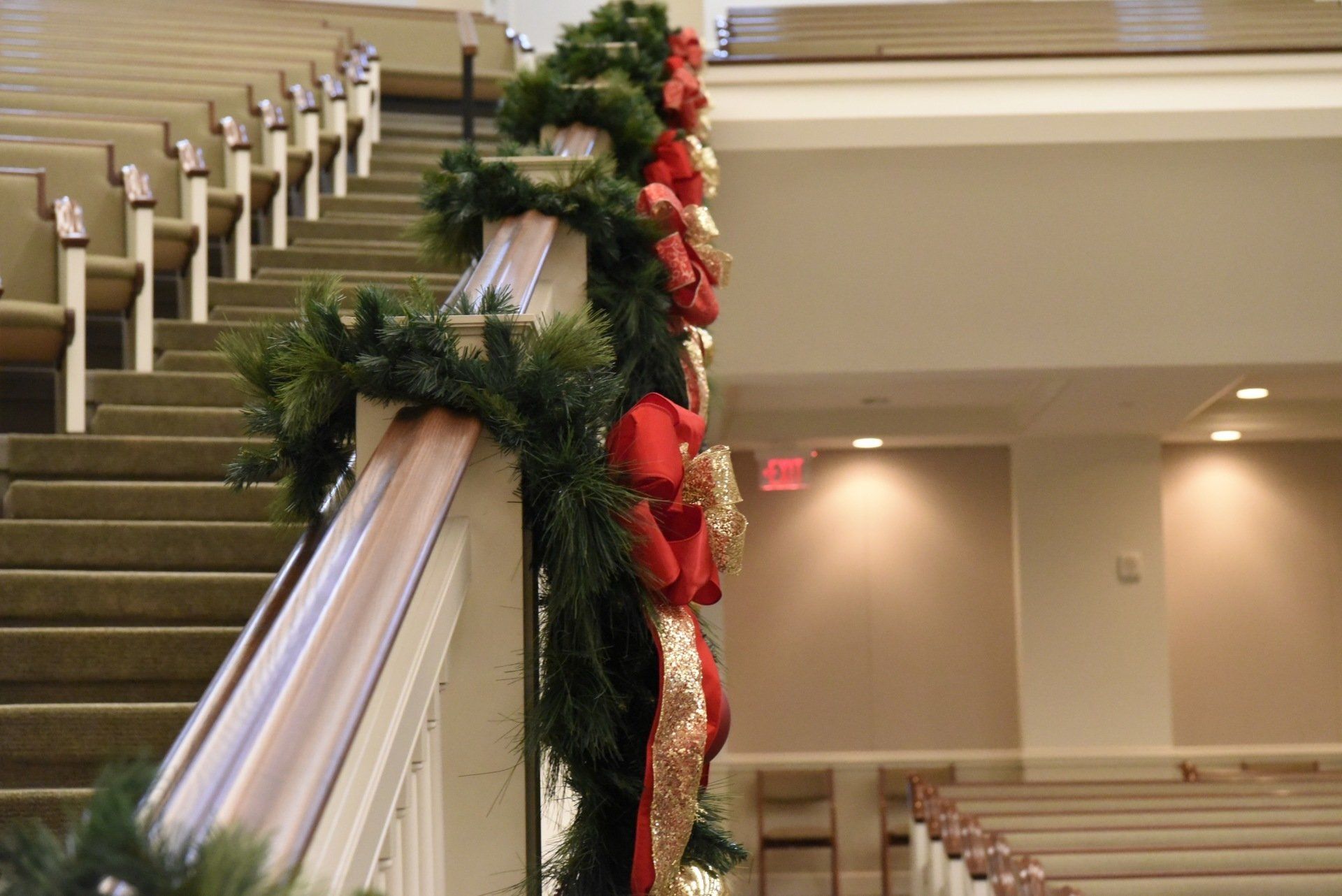Staircase in church decorated with green garland, red bows, and white ribbons for Christmas.