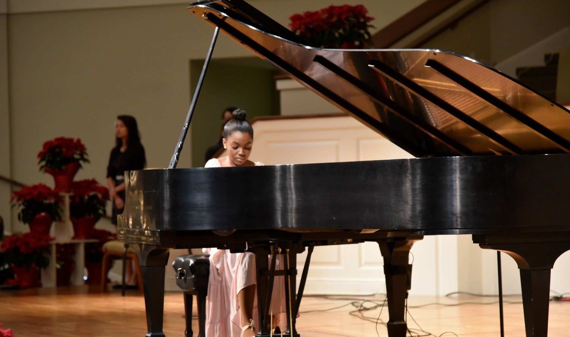 Young girl plays piano on a stage, wearing a pink dress.