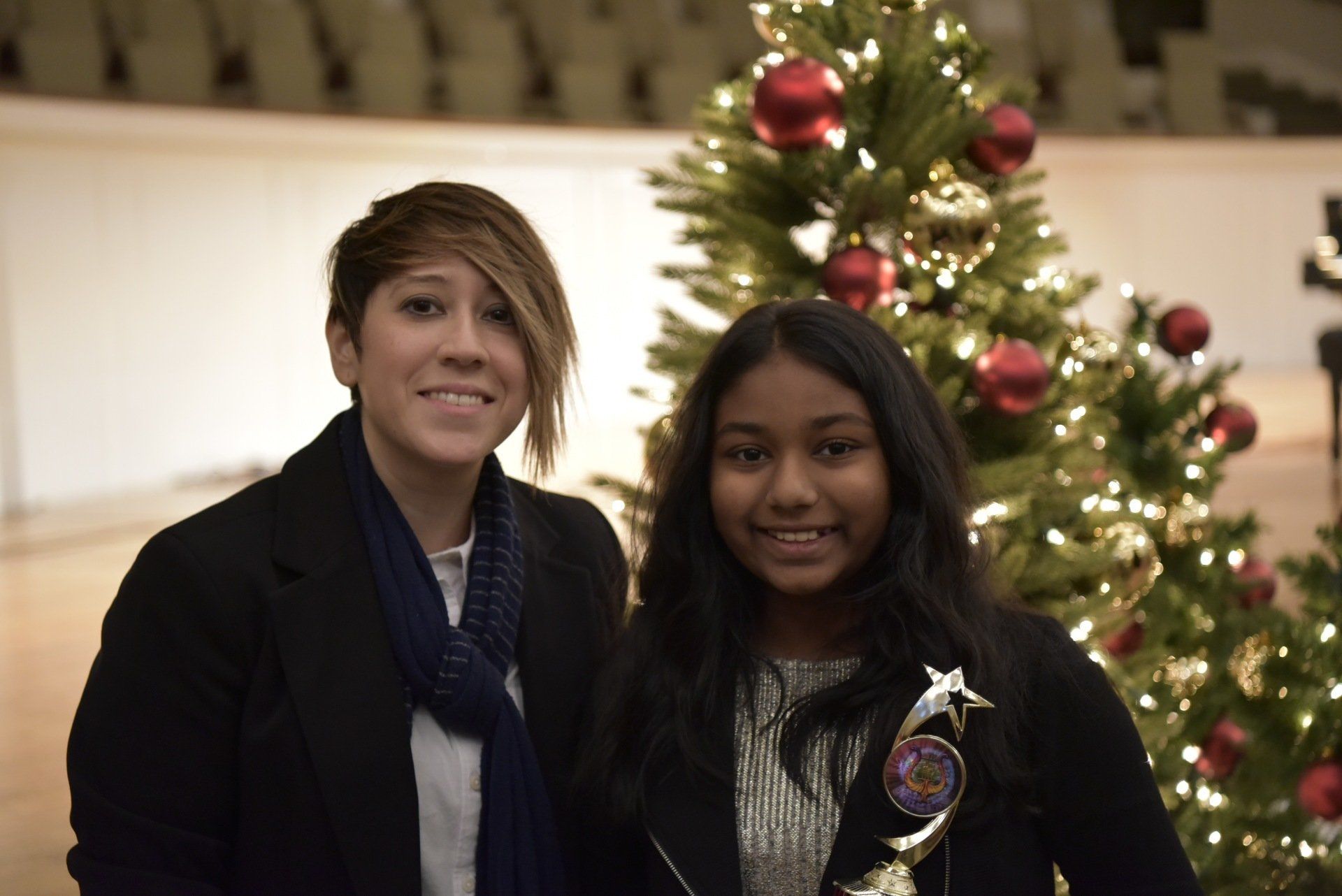 Two smiling people pose near a decorated Christmas tree. 