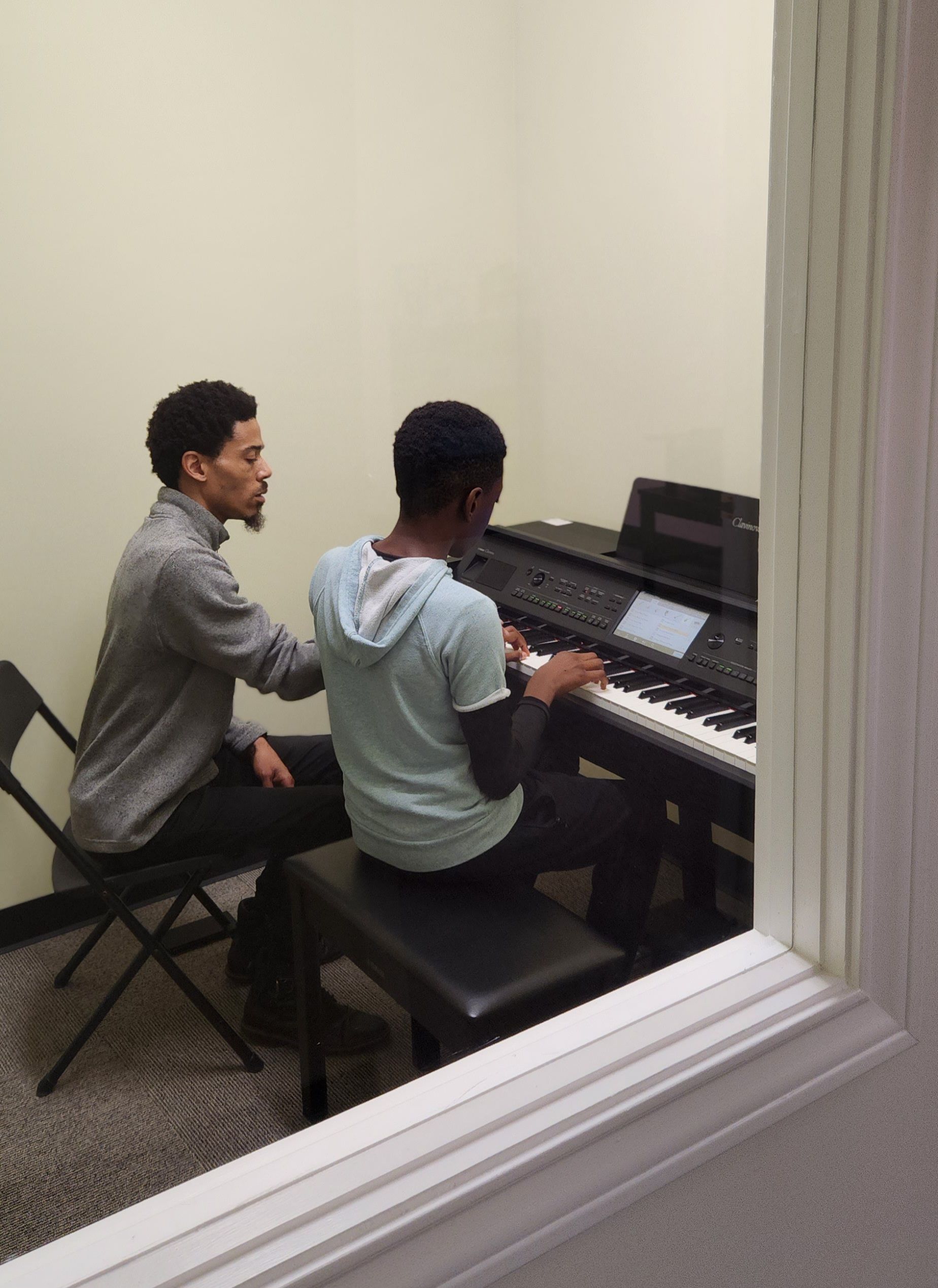Man teaching a student how to play a keyboard in a music room.