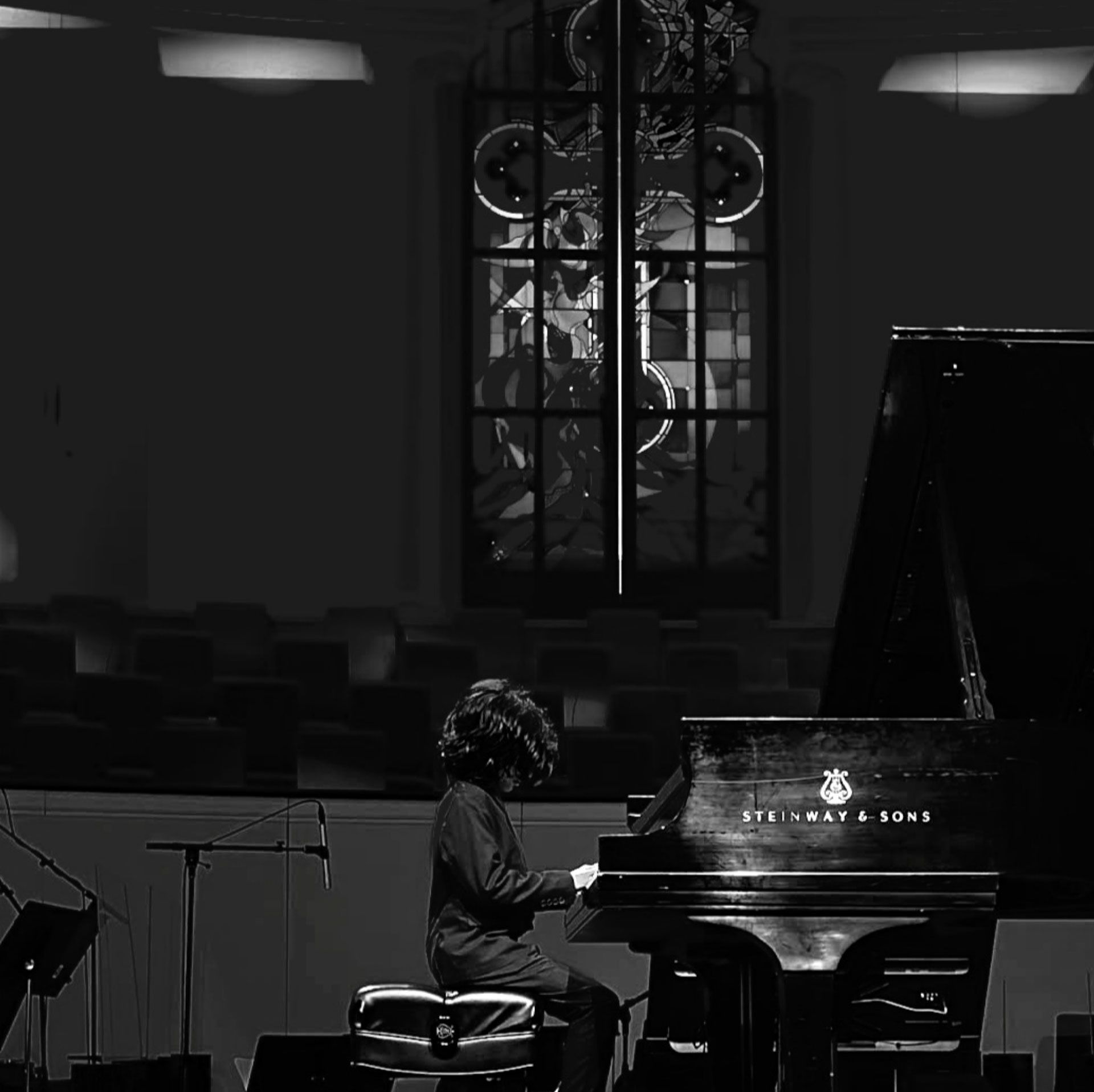 A pianist plays a grand piano in a dimly lit concert hall.
