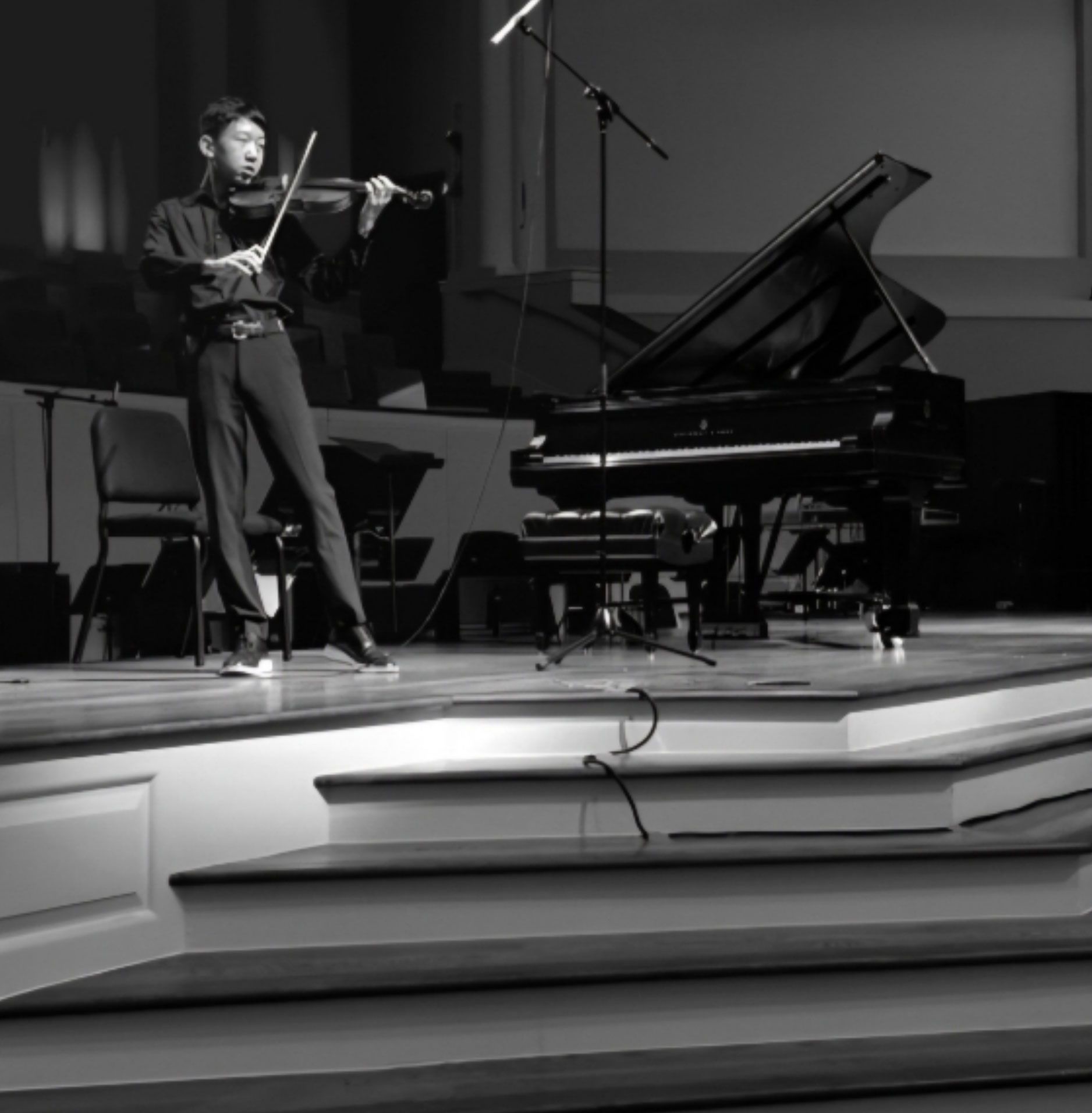 A man playing the violin on stage, next to a grand piano.