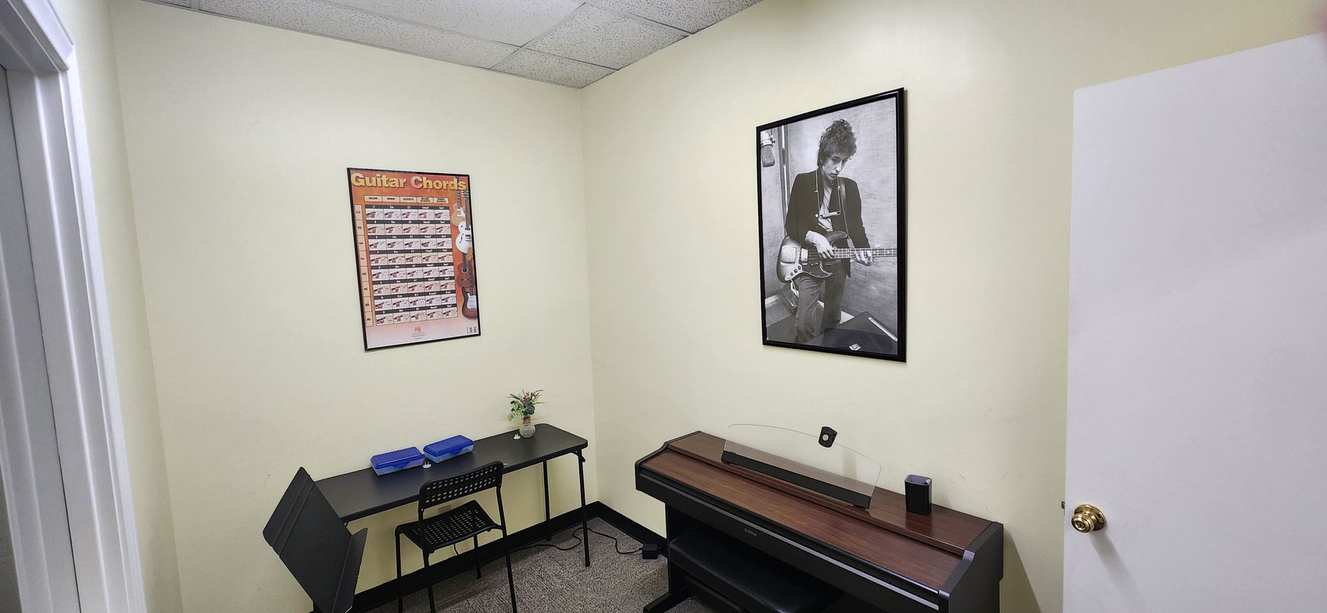 A music room with a piano, framed photos, and a small desk.