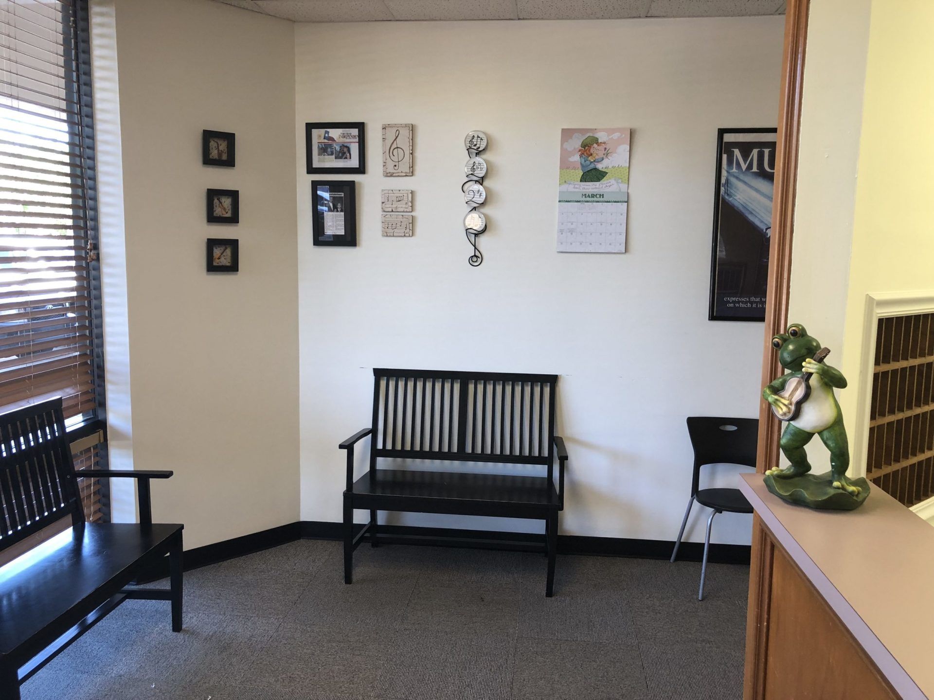Waiting room with black benches, artwork, and a frog statue on the counter.