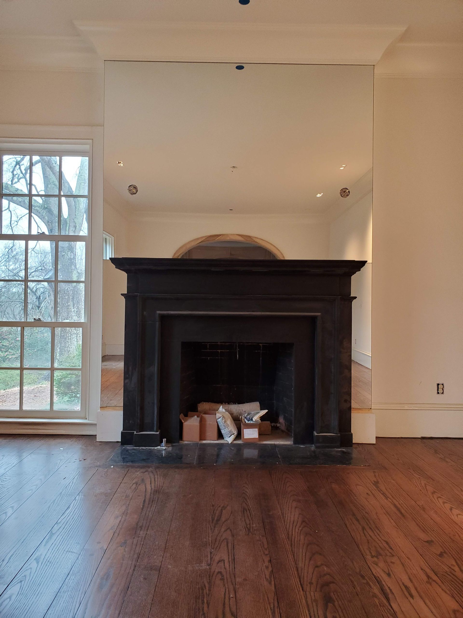 Empty room with a dark fireplace, white walls, hardwood floors, and a large window on the left