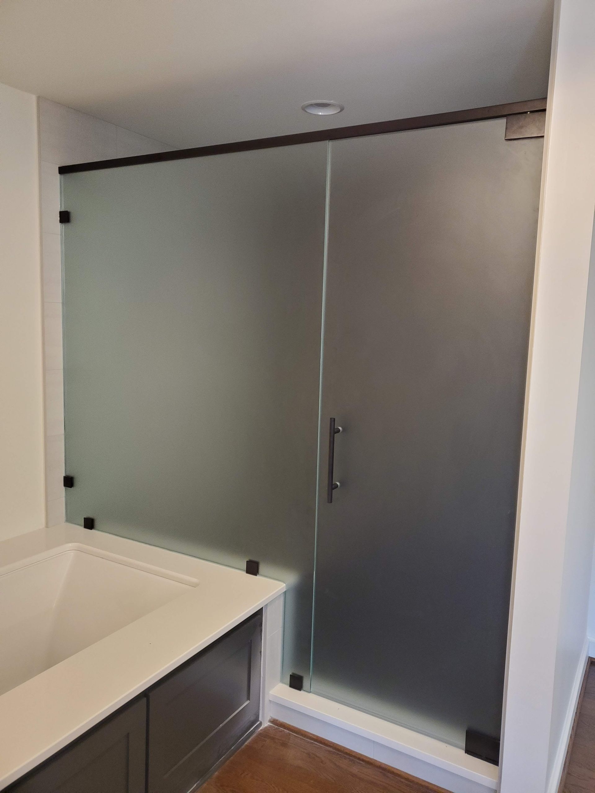 Frosted glass shower enclosure with gray doors beside a white bathtub in a bathroom