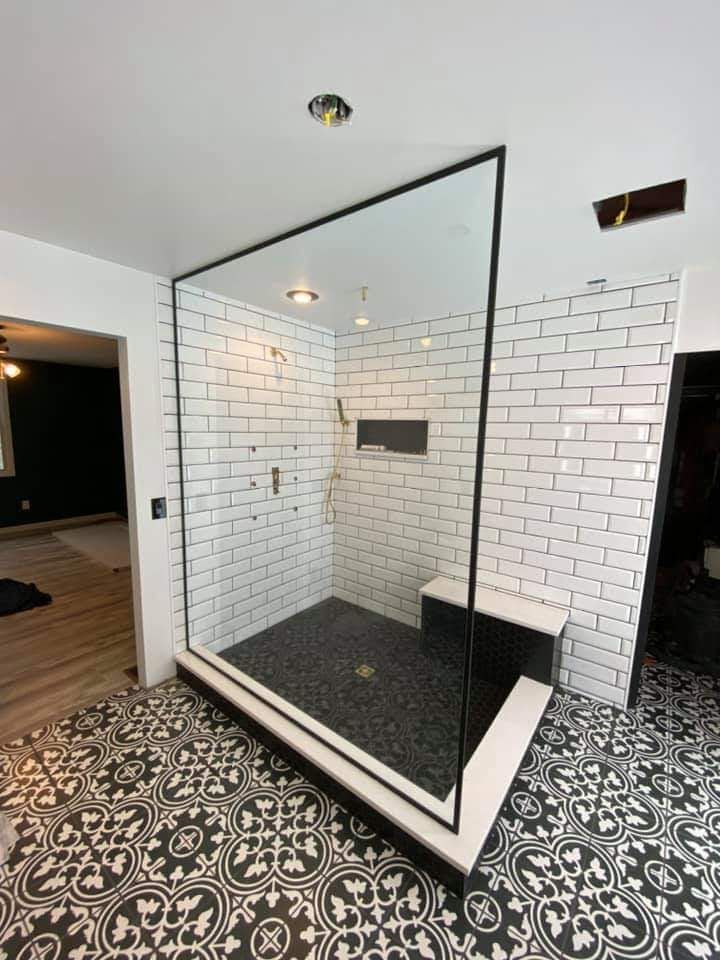 Modern shower with black-framed glass enclosure, white subway tile, and patterned floor tile in a bathroom