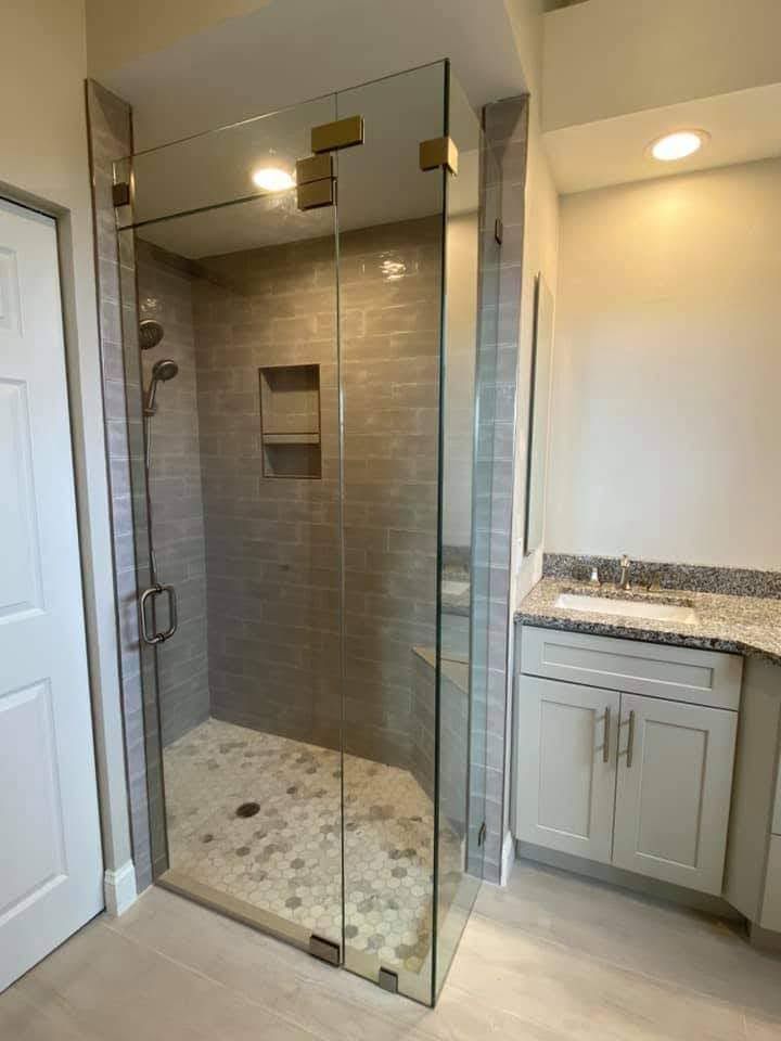 Glass walk-in shower beside a vanity in a modern beige-tiled bathroom.