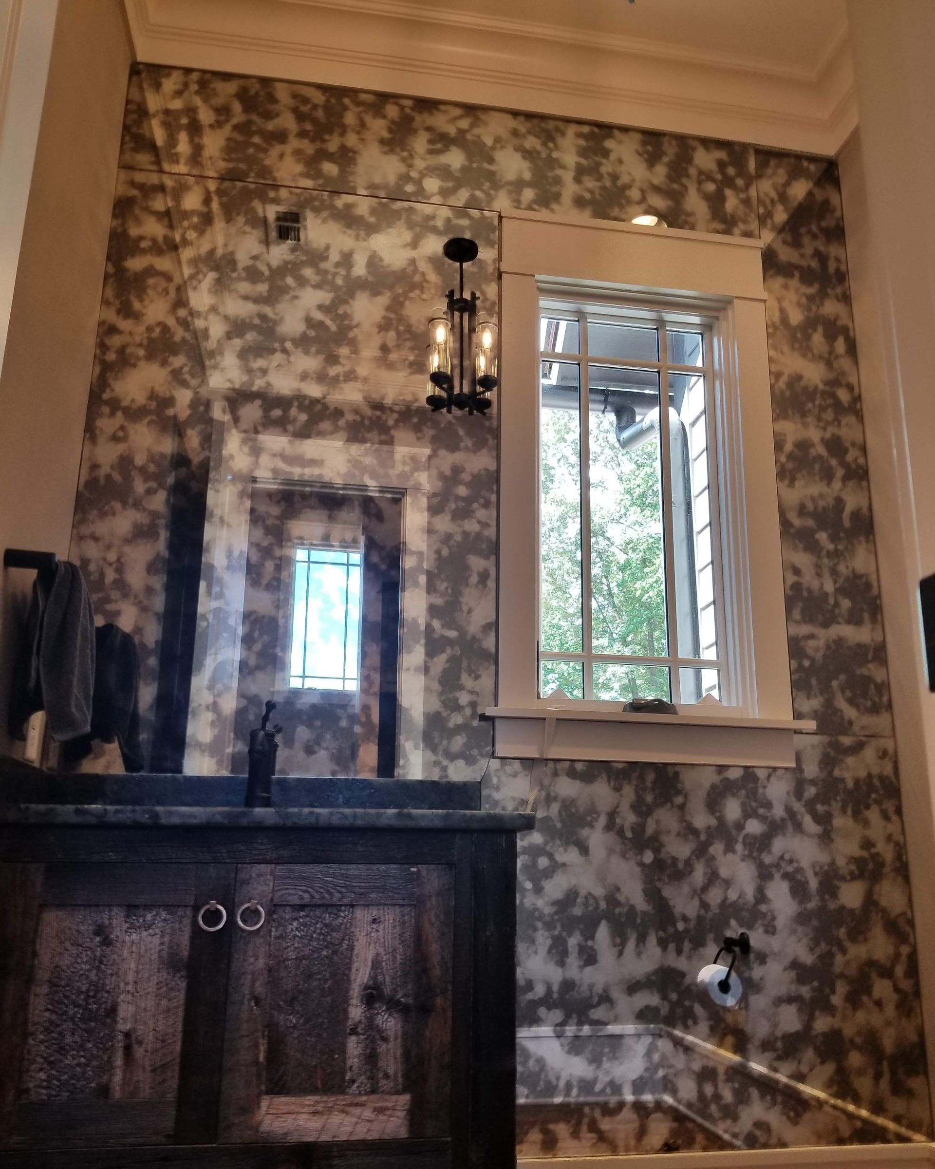 Dim room with mottled wallpaper, a dark fireplace, and a white-framed window looking out to trees.