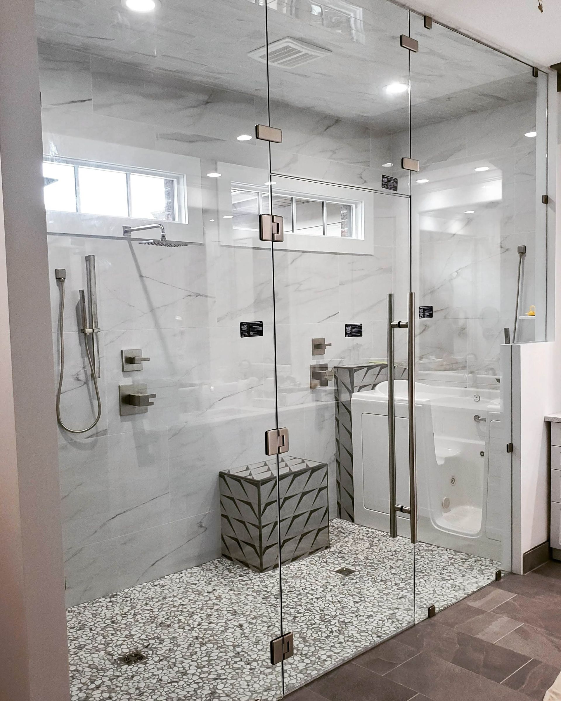 Modern glass shower with white tiled walls, pebble floor, and chrome fixtures in a bathroom