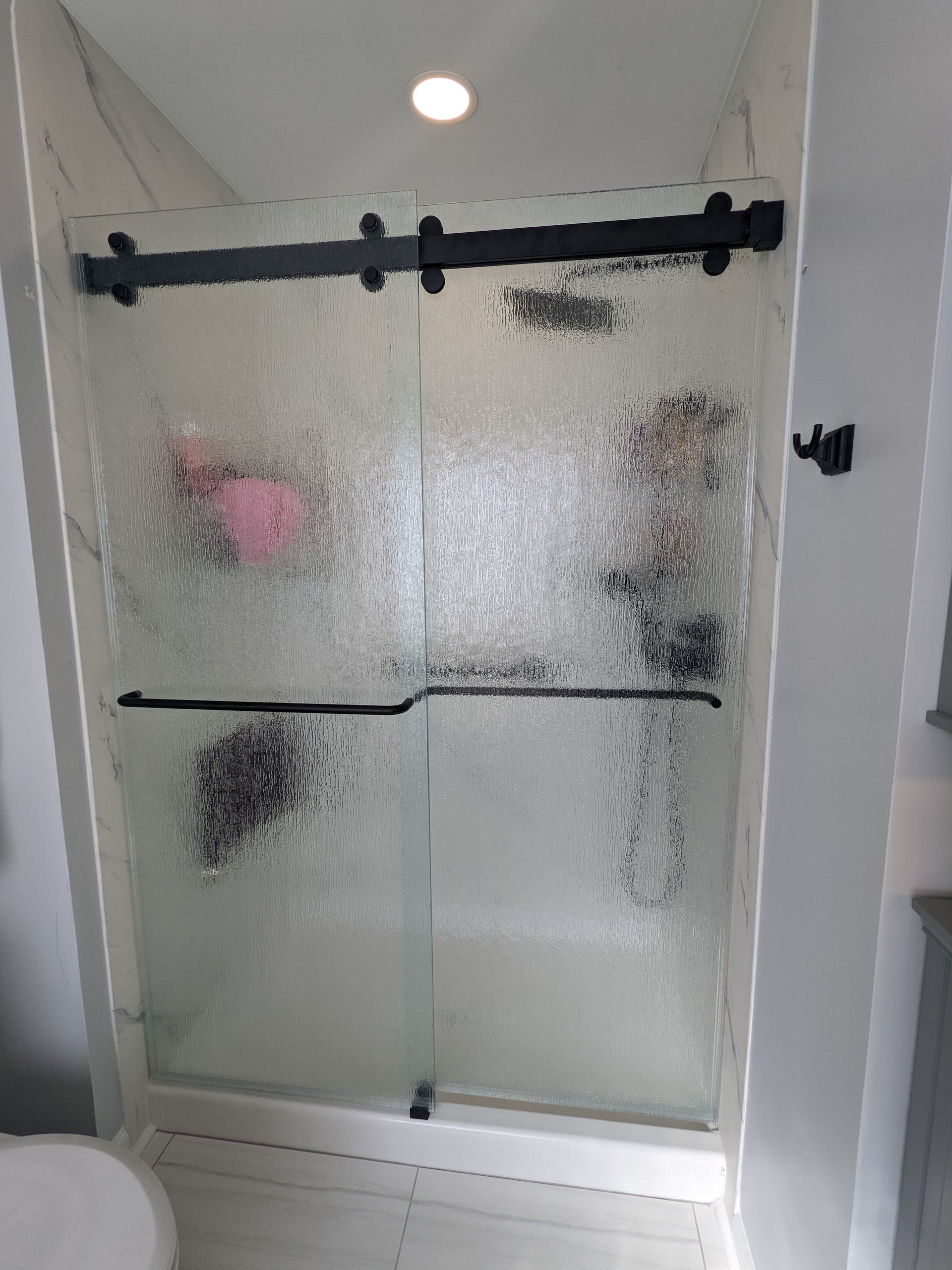 Glass shower enclosure with black hardware and frosted shower doors in a bright bathroom