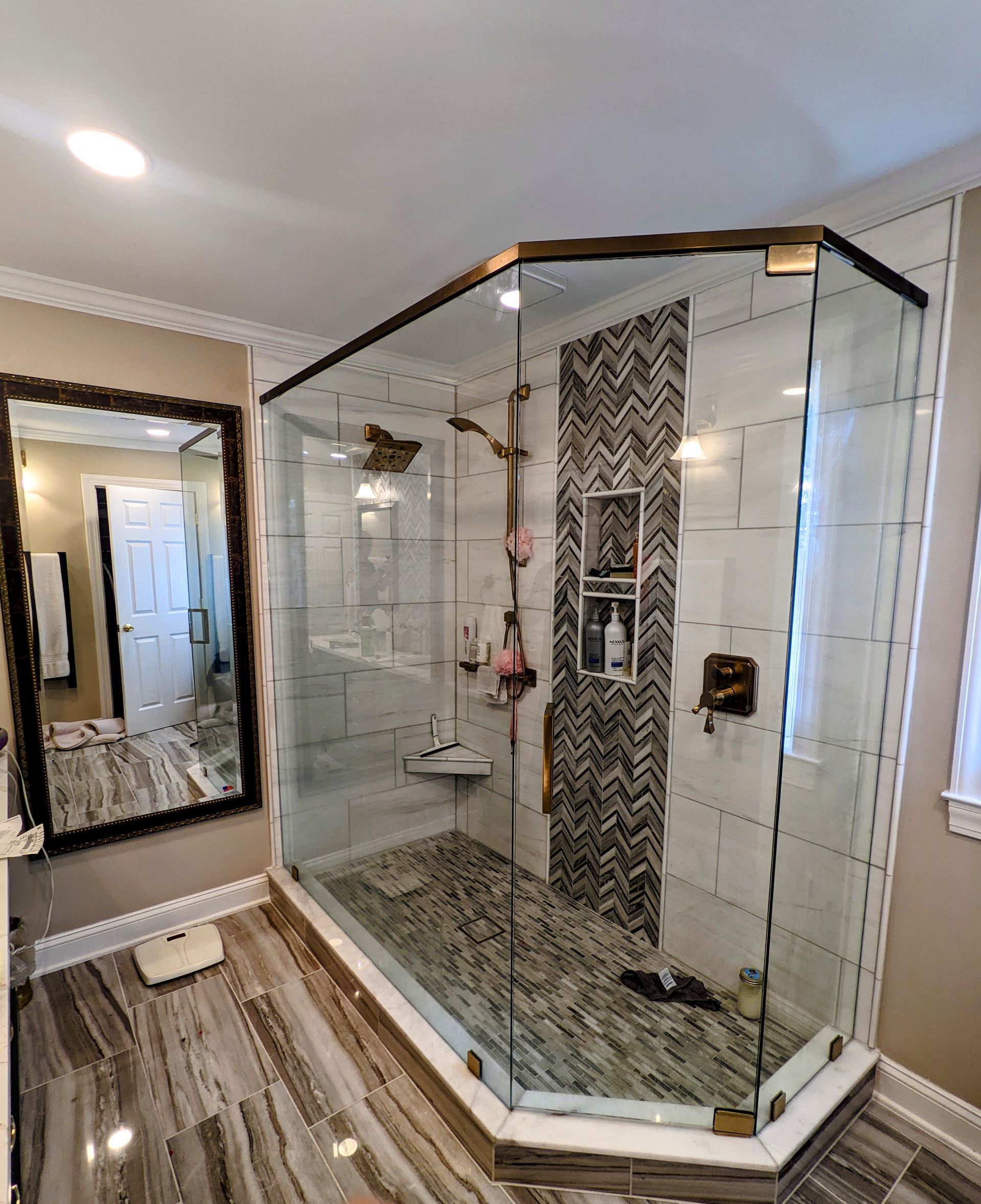 Glass walk-in shower with patterned tile, white walls, and wood-look floor in a bathroom