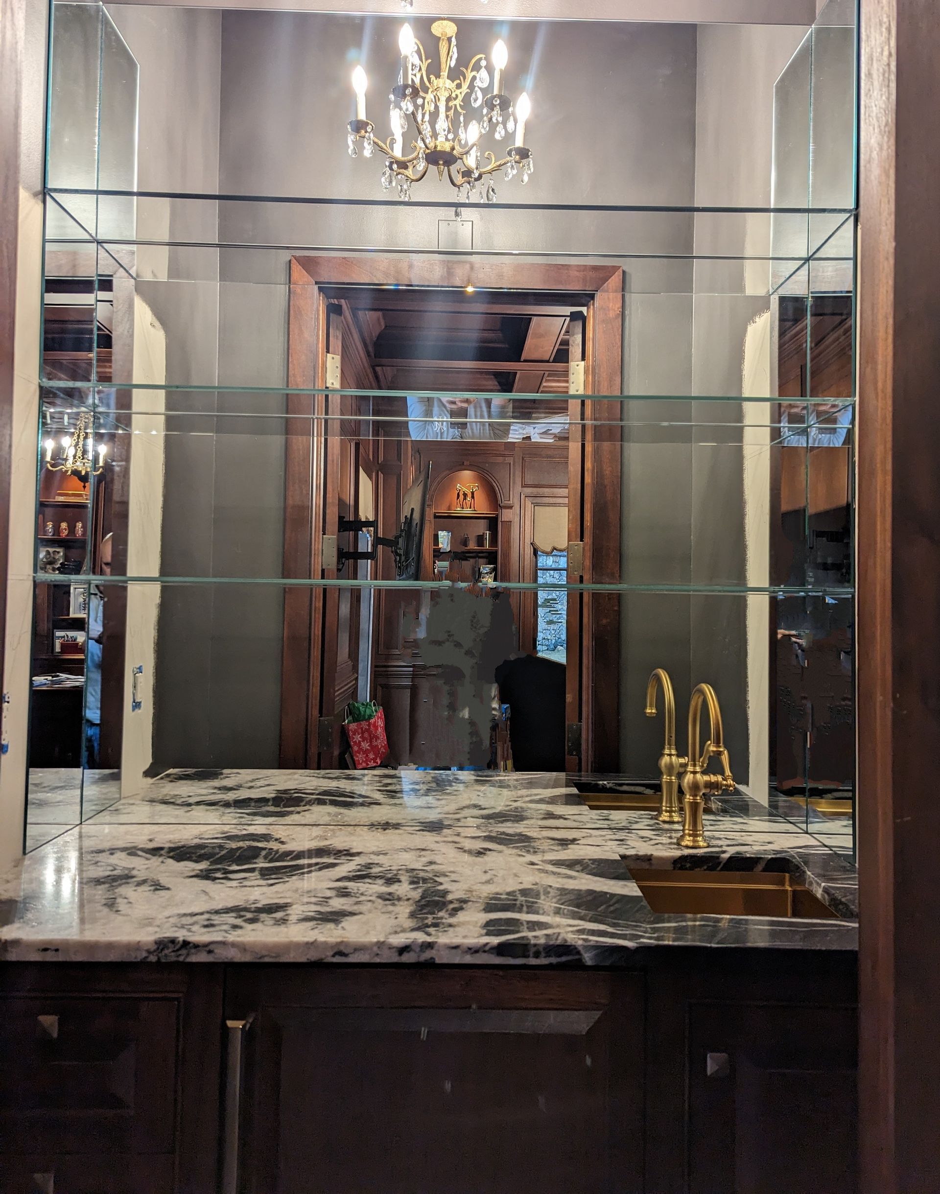 Elegant hotel lobby mirror with chandelier, dark wood counter, marble top, and gold fixtures
