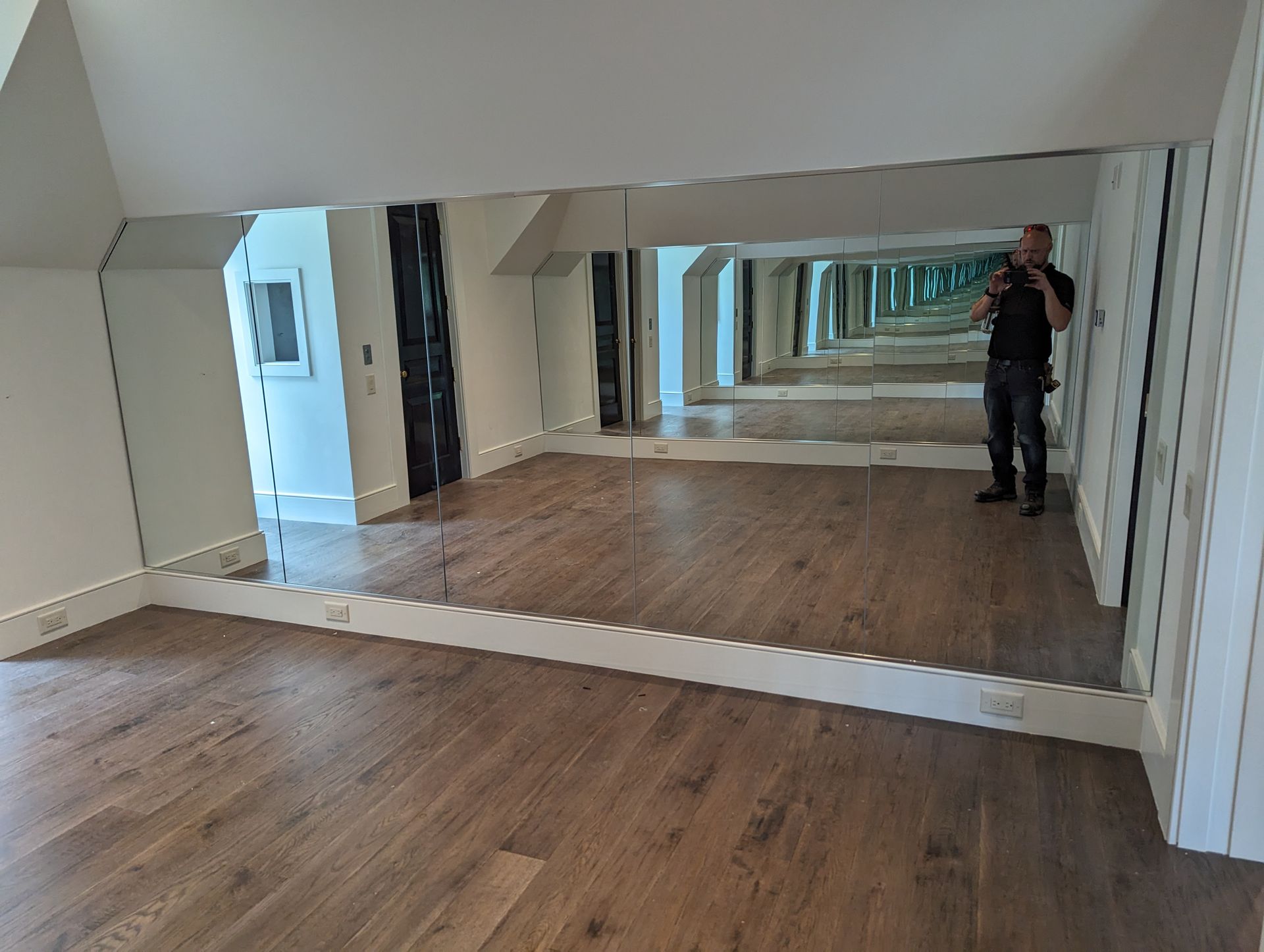 Mirror-lined room with wood floors and a person standing at the far right