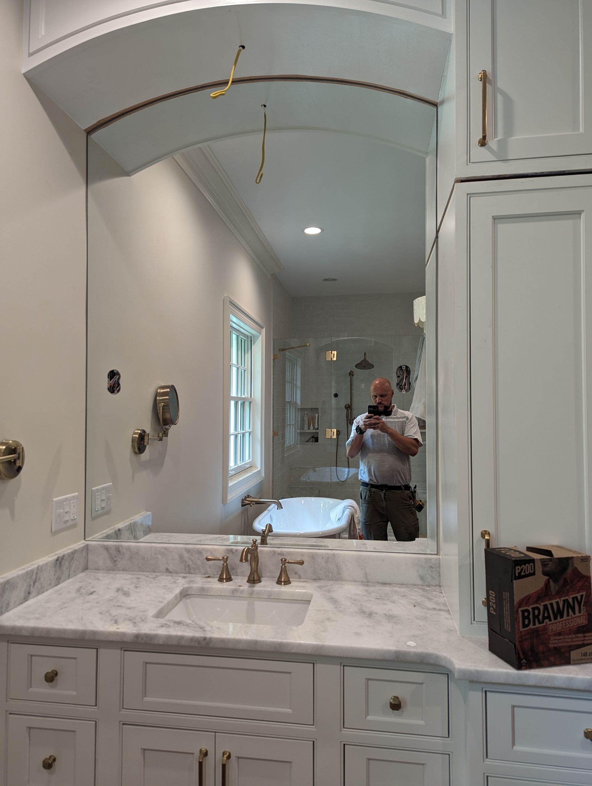 Bathroom vanity with white marble countertop, arched mirror, and a person taking a photo reflected in the mirror.