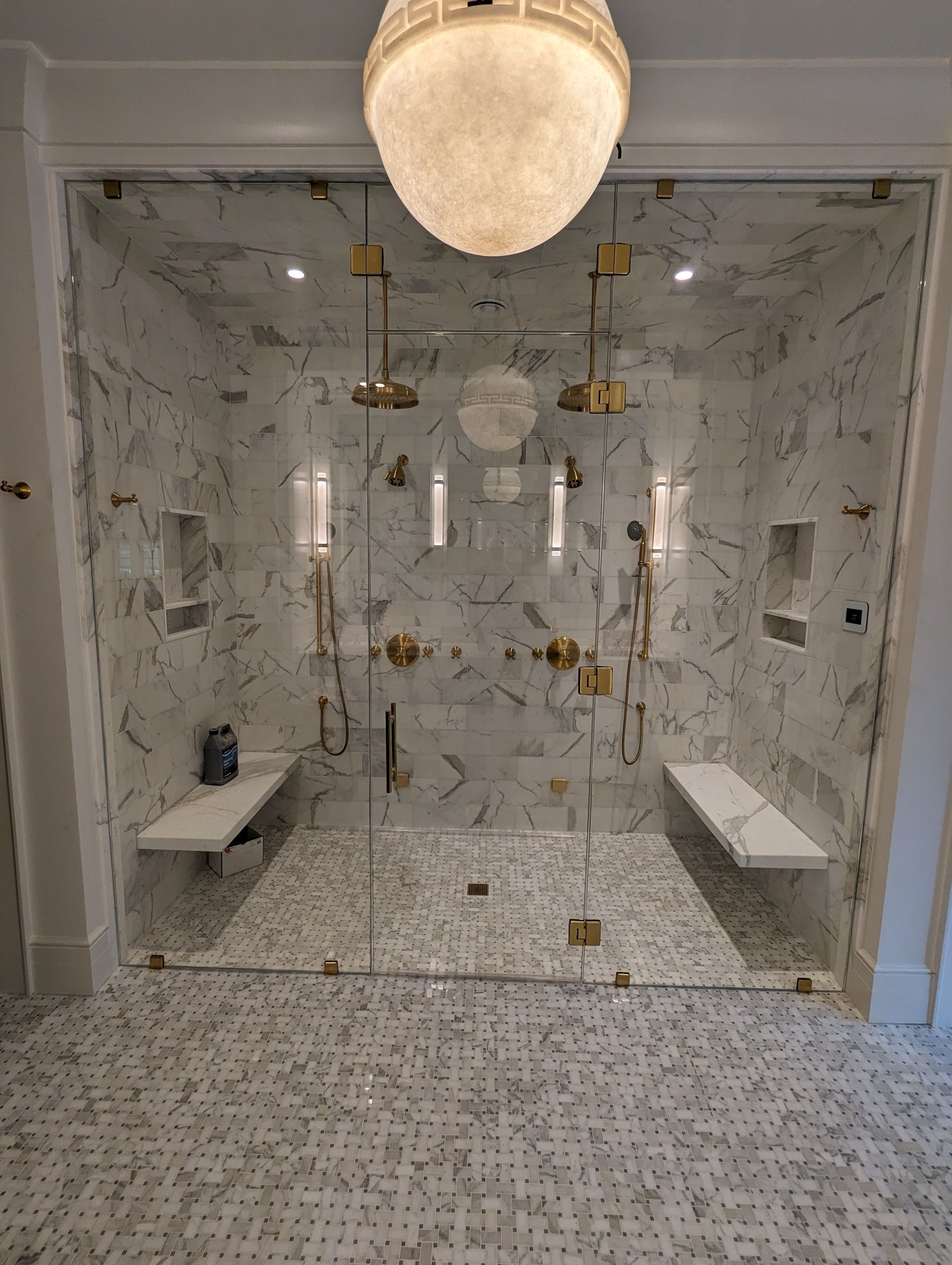 Marble bathroom with glass-enclosed shower, gold fixtures, and mosaic tile floor