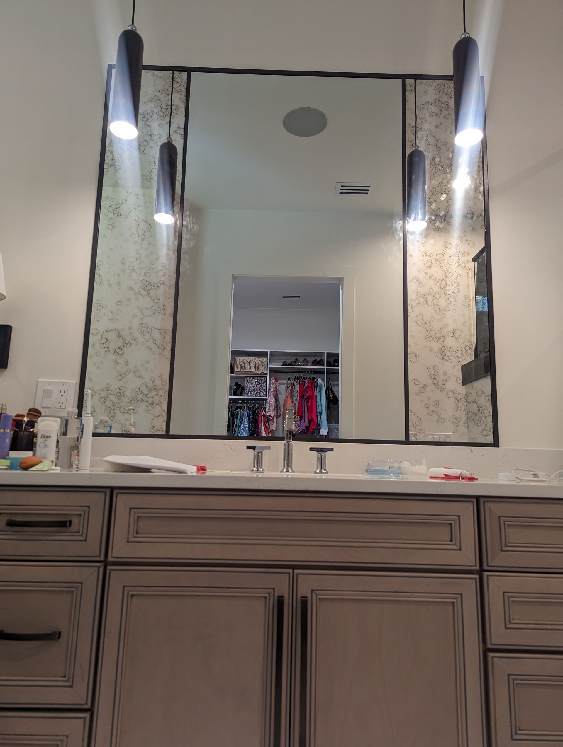 Bathroom vanity with large mirror, dual wall sconces, and open closet reflected in the center.