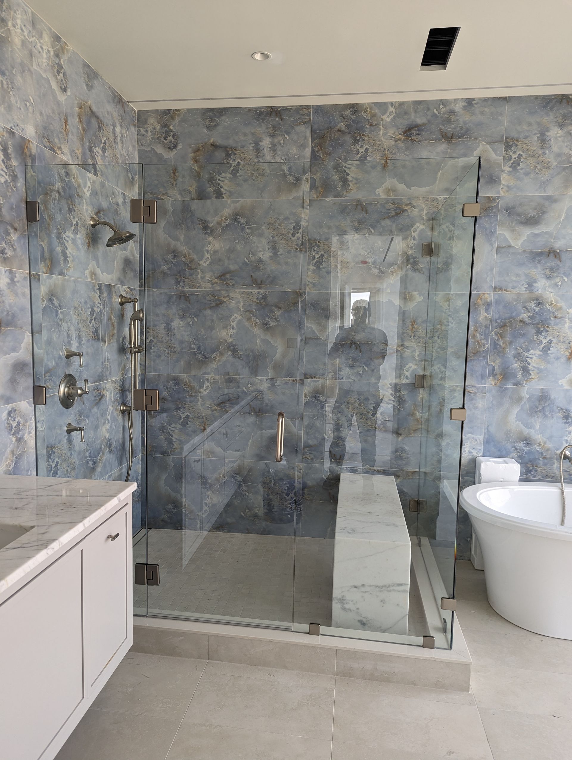 Modern bathroom with glass shower, gray stone walls, white vanity, and toilet