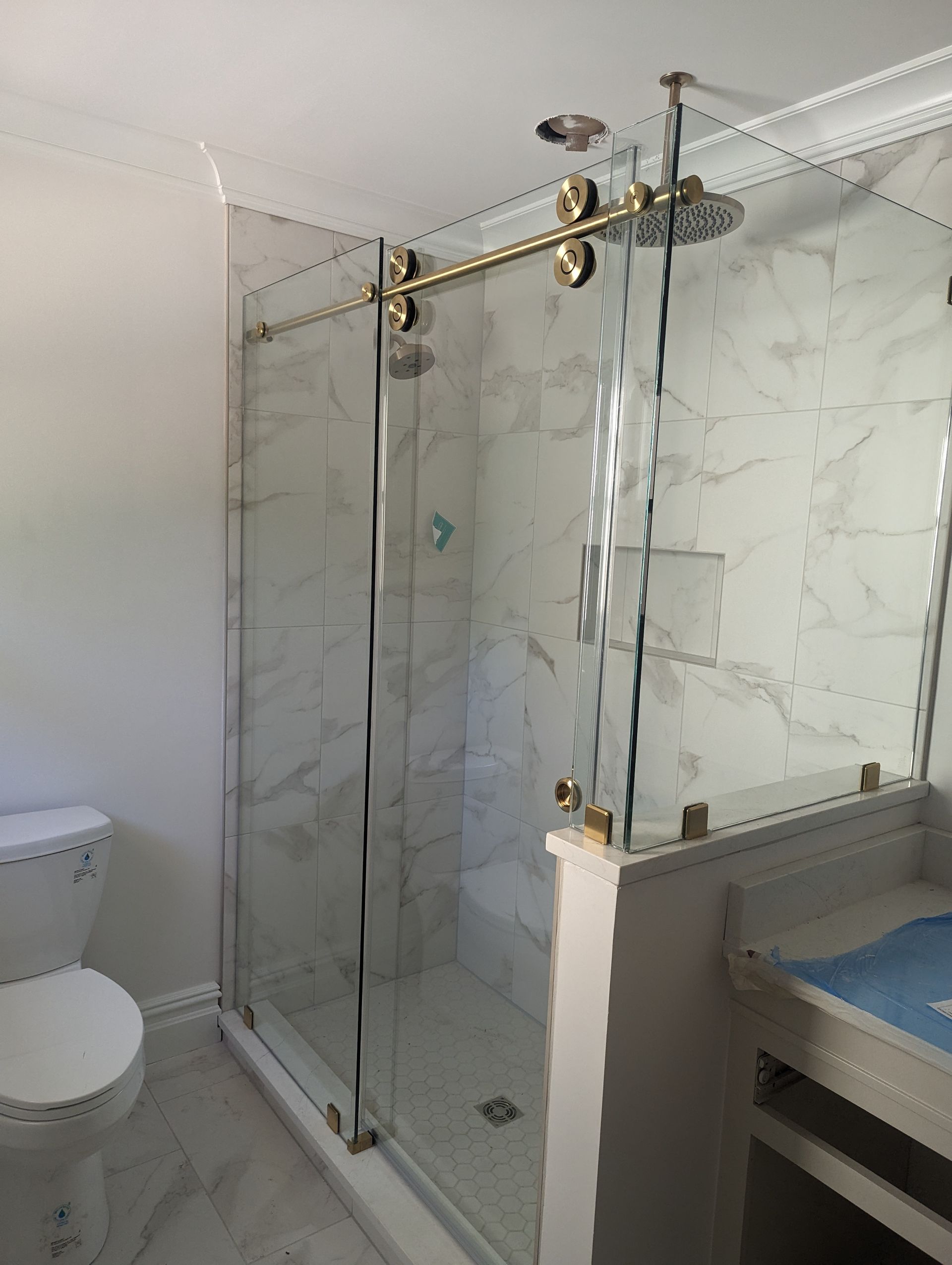 Bathroom with glass shower enclosure, brass fixtures, toilet, and vanity sink.