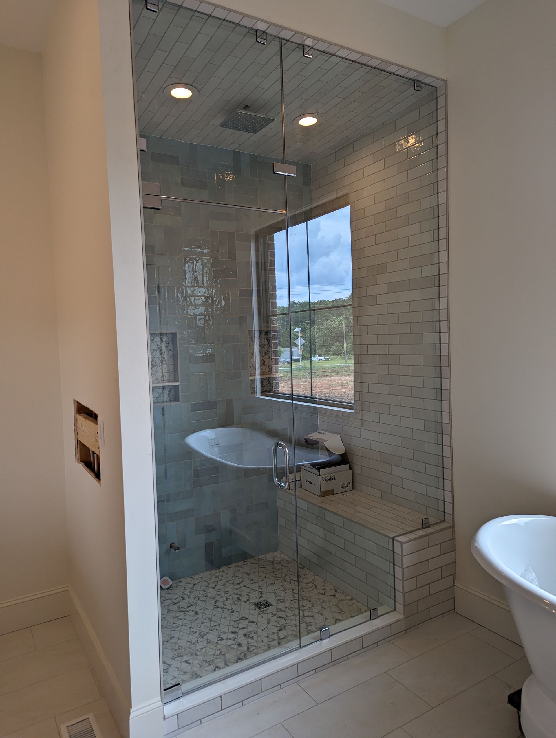 Glass walk-in shower with mosaic tile, white fixtures, and a window view beyond