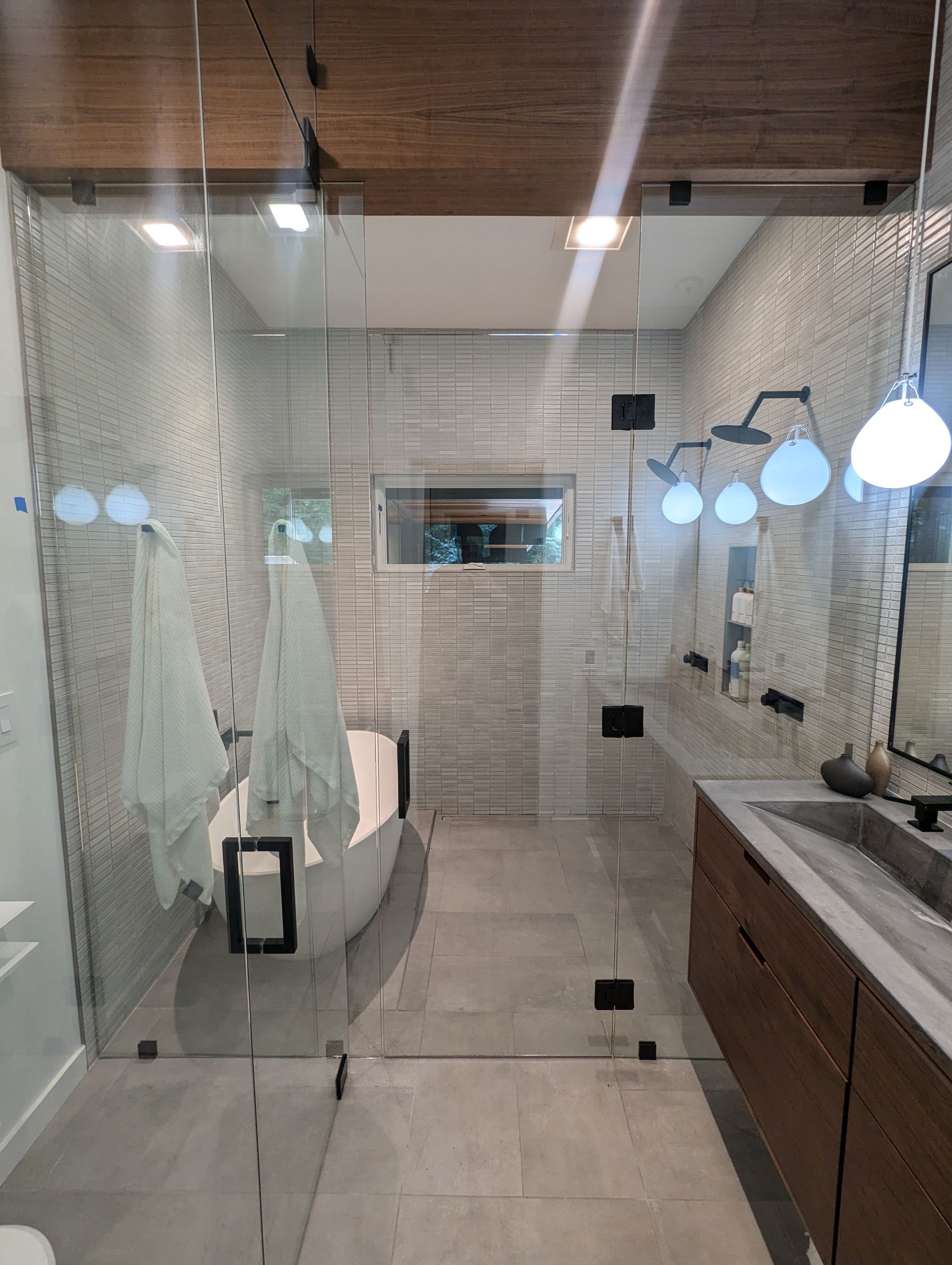 Modern bathroom with glass shower, freestanding tub, double vanity, and wood-accent ceiling