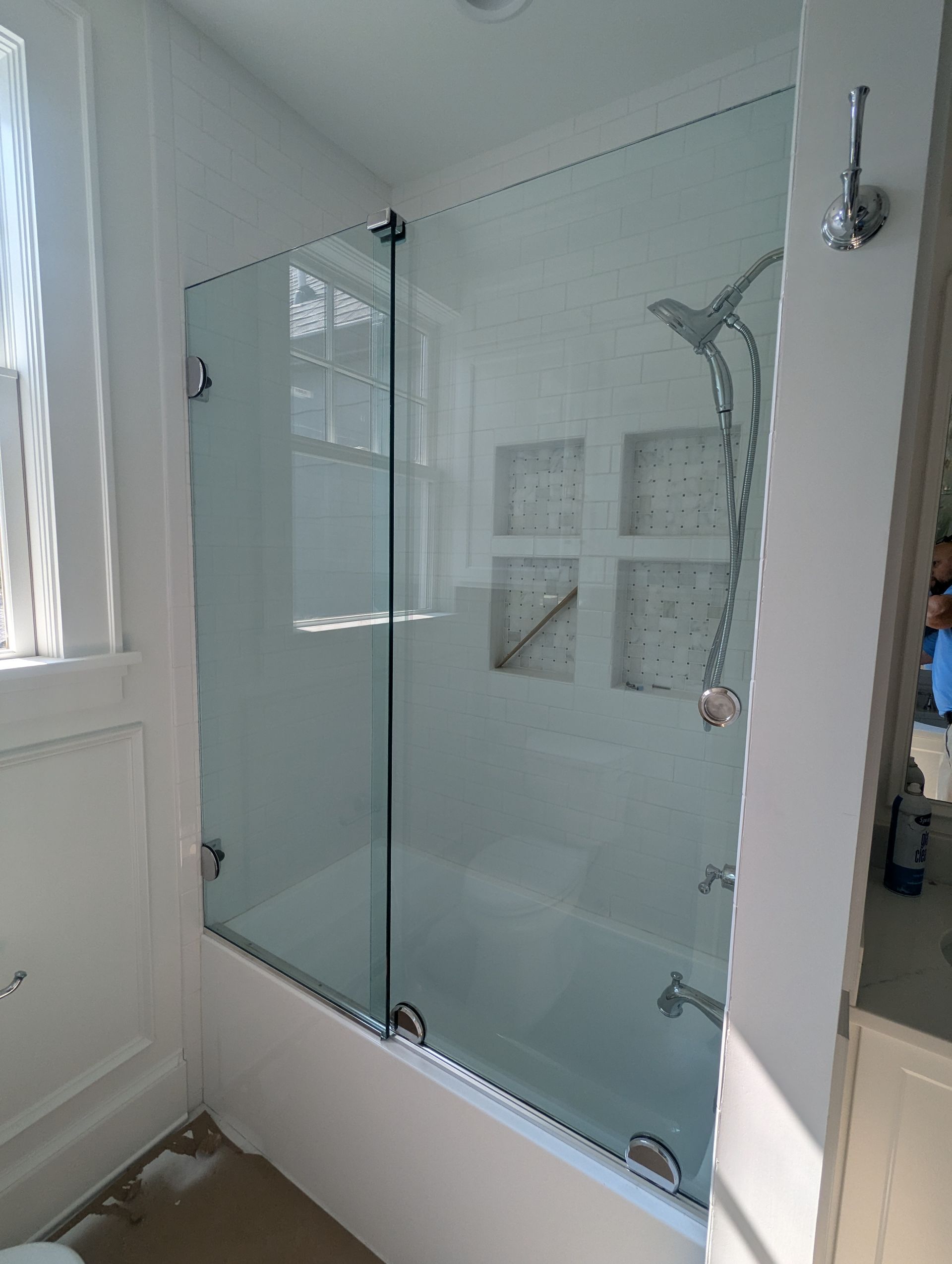 Glass-walled bathtub and shower in a bright white bathroom with a window.