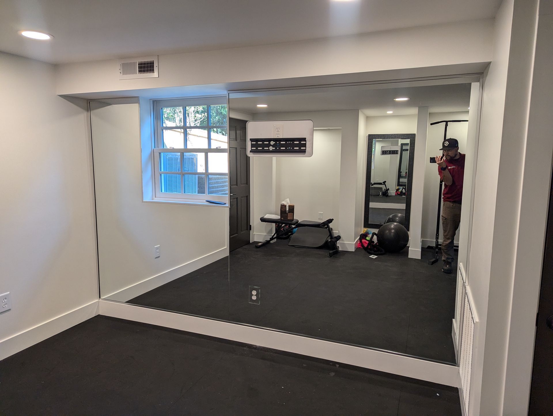 Home gym room with wall mirror, black exercise mat, and workout equipment near a window