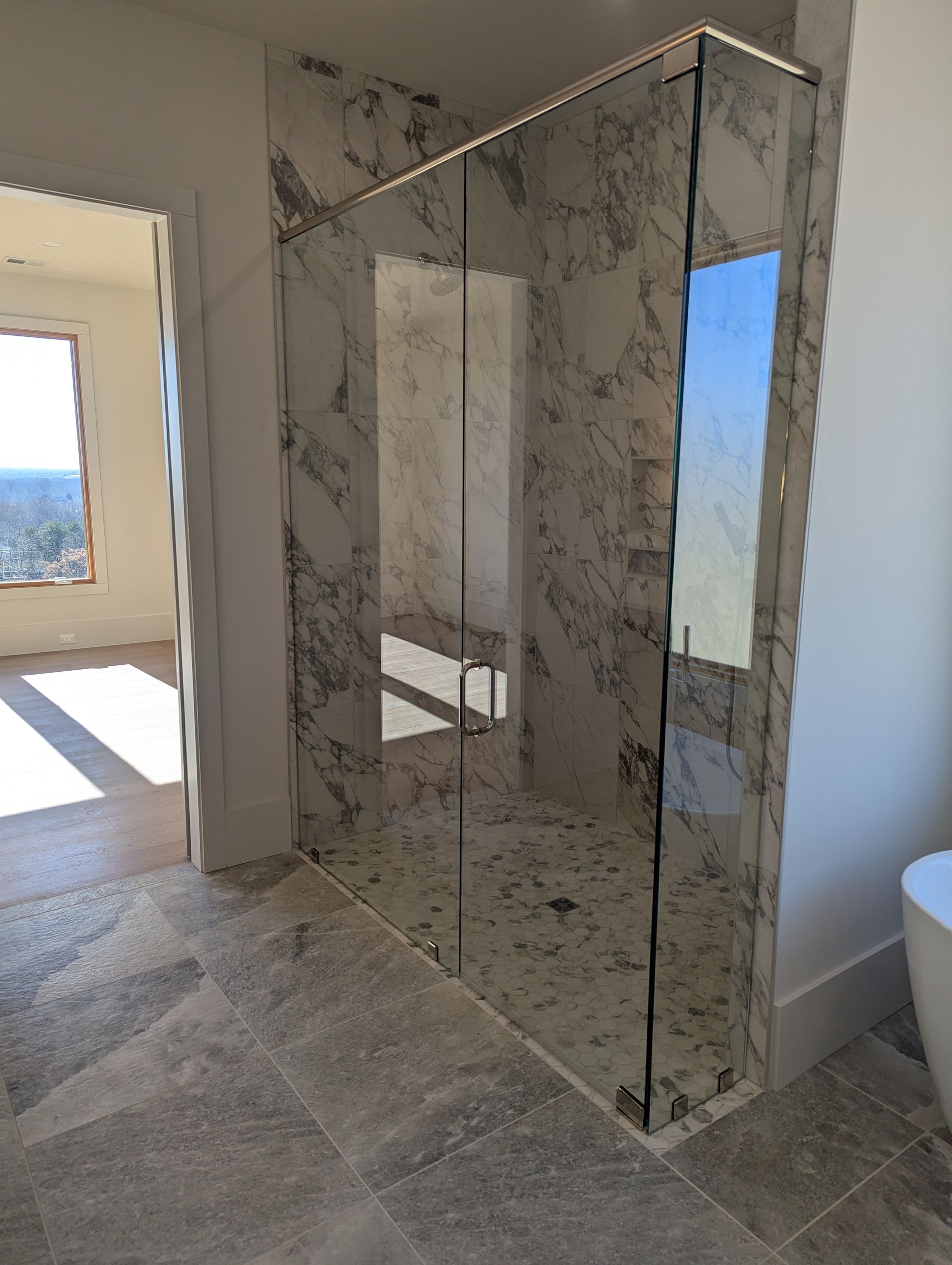 Marble-clad shower room with glass enclosure and tiled floor near a bright window