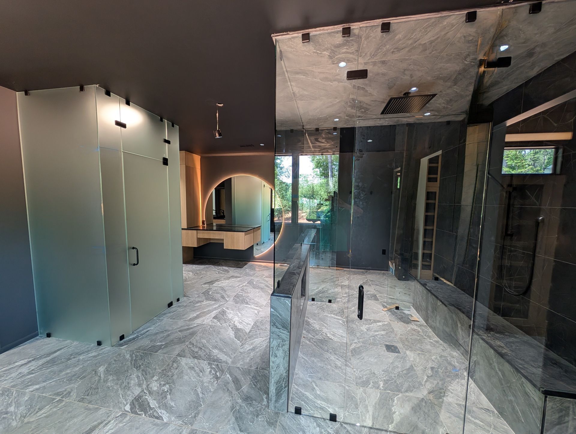 Modern bathroom under renovation with glass shower partitions, frosted cabinets, and marble flooring