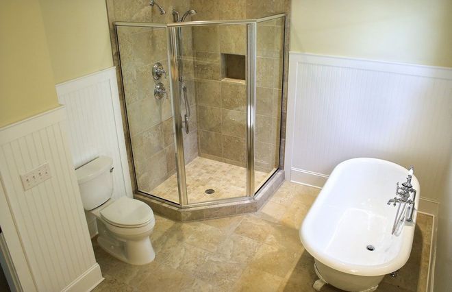 Bathroom with shower, toilet, and freestanding bathtub on beige tile floor.