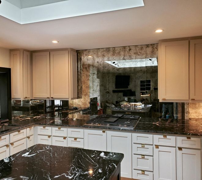 Modern kitchen with cream cabinets, dark granite counters, and a large mirrored backsplash