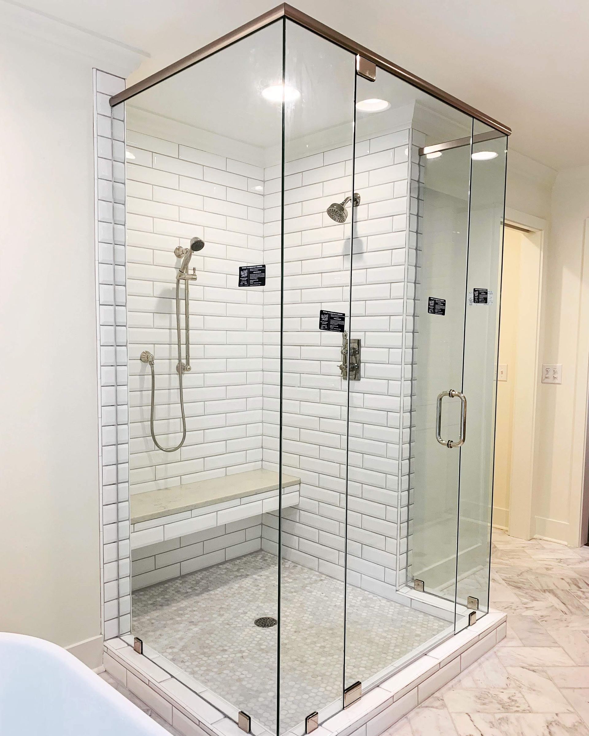 Glass walk-in shower with chrome fixtures, white subway tile walls, and marble-look floor.
