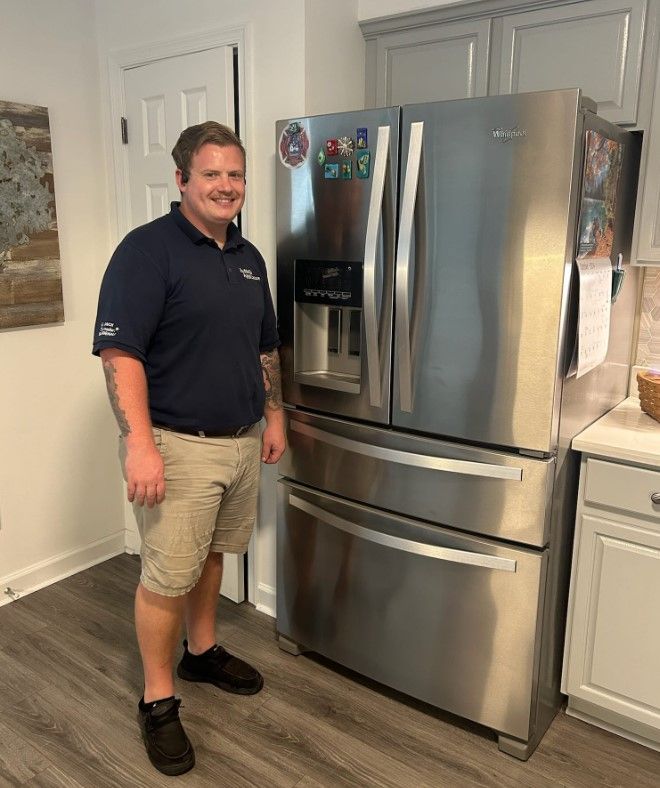 Man in navy polo stands beside a stainless steel Whirlpool fridge in a kitchen.