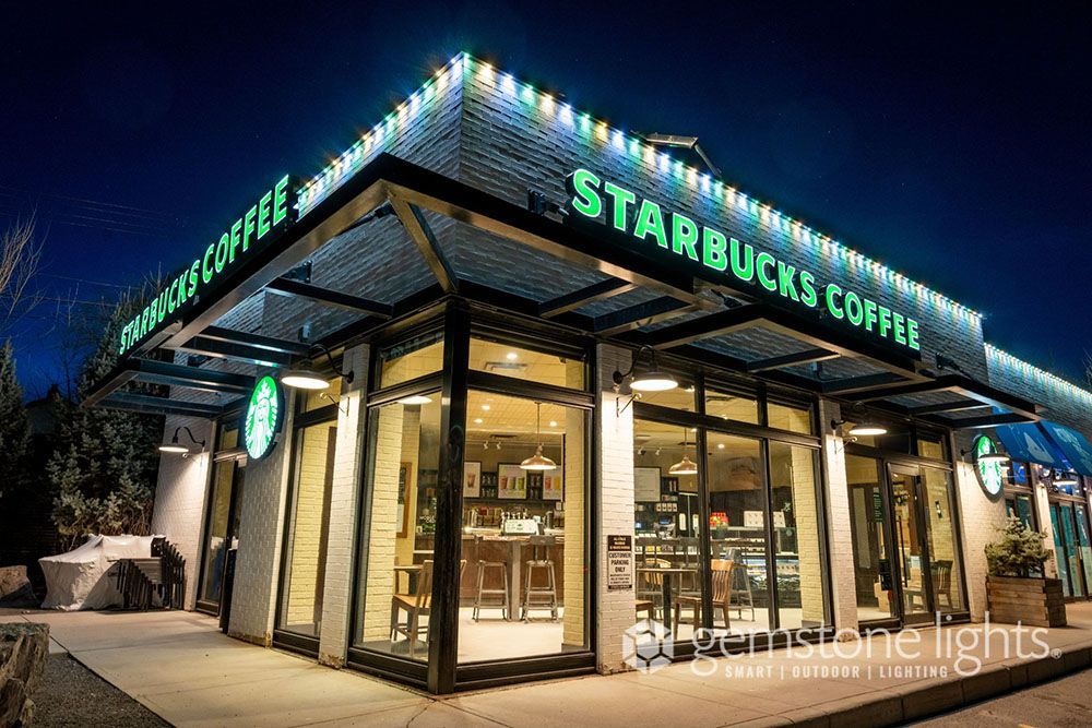A starbucks coffee shop is lit up at night with christmas lights.