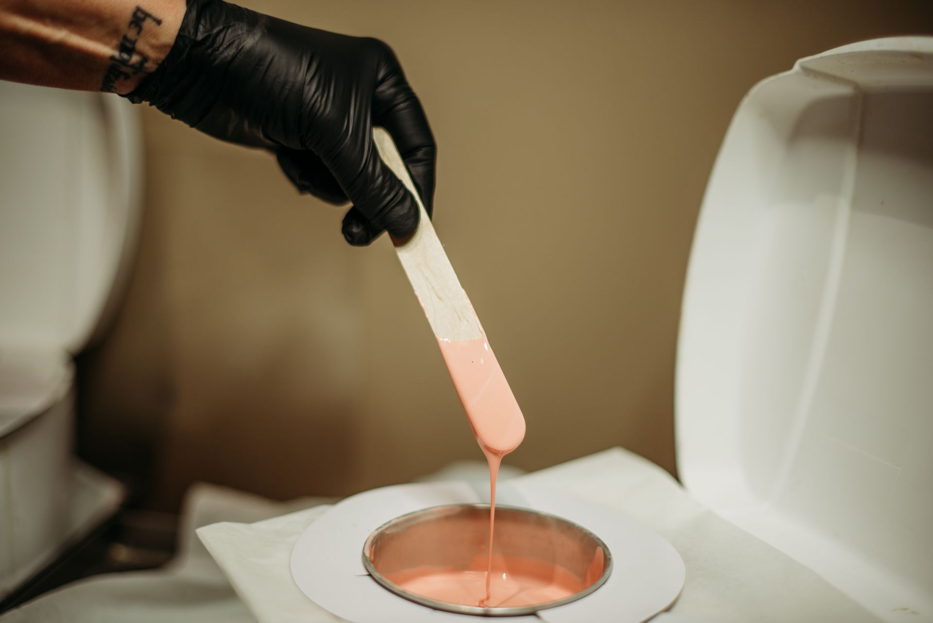 A person wearing black gloves is waxing their hair with a stick.