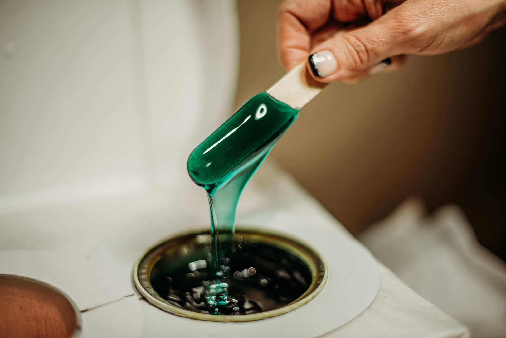A person is pouring wax into a can with a stick.