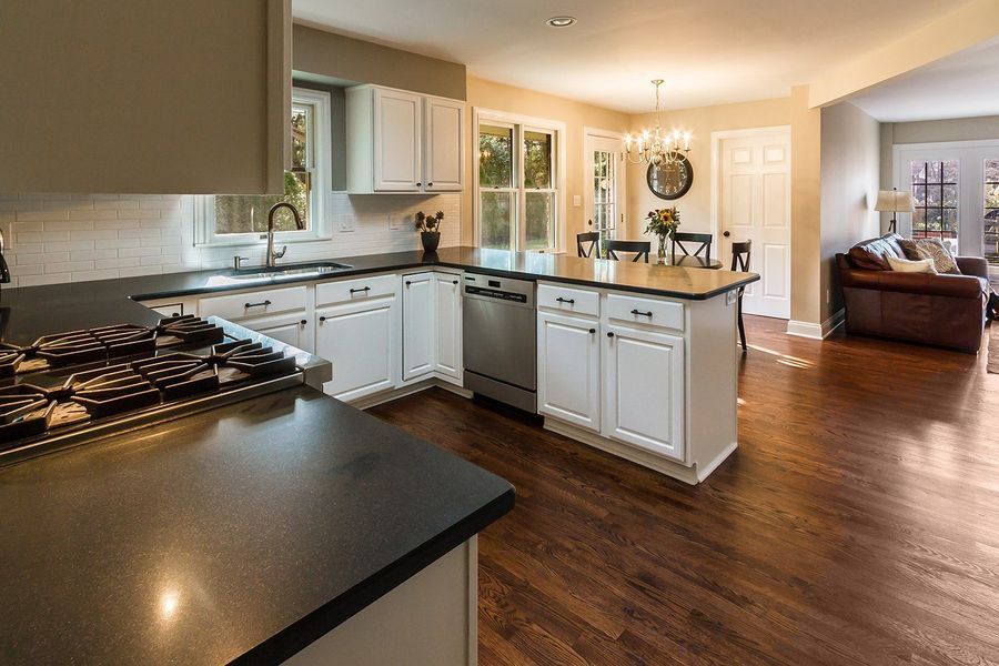 L-shaped kitchen with white cabinets, dark countertops, stainless steel appliances, and dark hardwood floors.