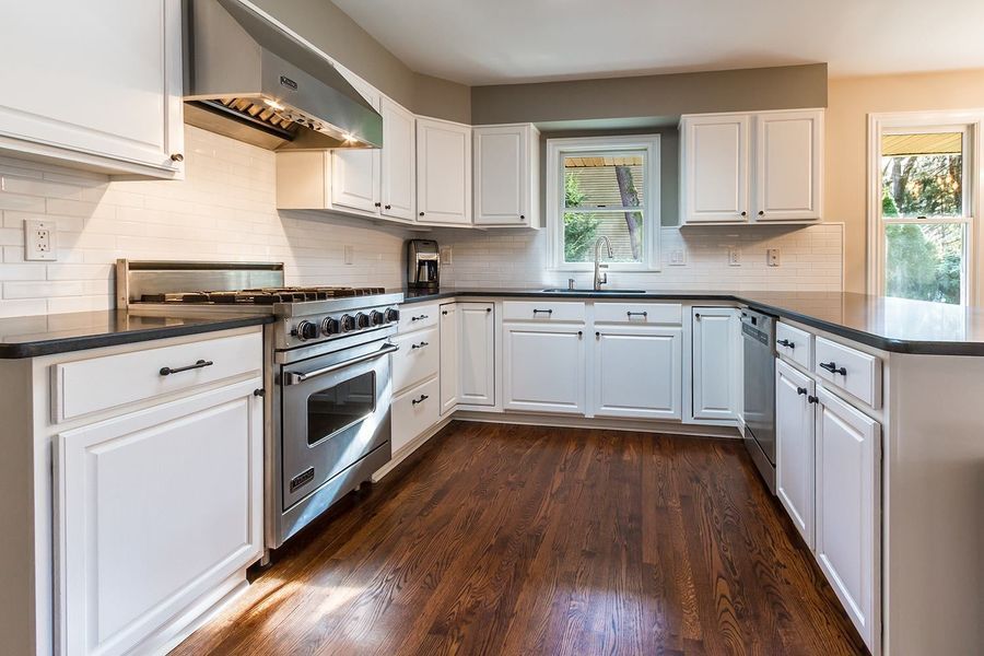 Bright white kitchen with stainless steel appliances, dark countertops, and hardwood floors.