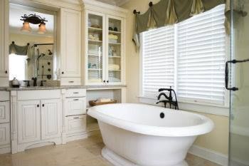 Elegant white bathroom with freestanding tub, built-in cabinetry, and window with blinds.