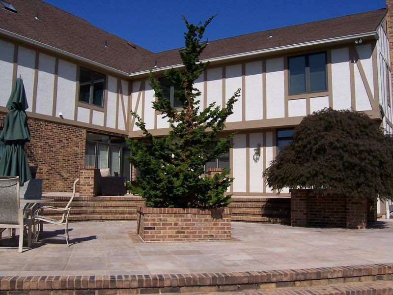 Two-story house with brown roof and white siding, a small tree, and patio.
