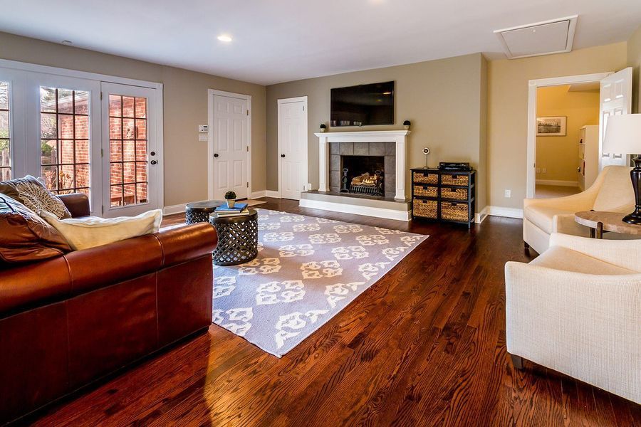 Living room with fireplace, hardwood floors, and patterned rug. Leather sofa, white armchairs, and french doors.
