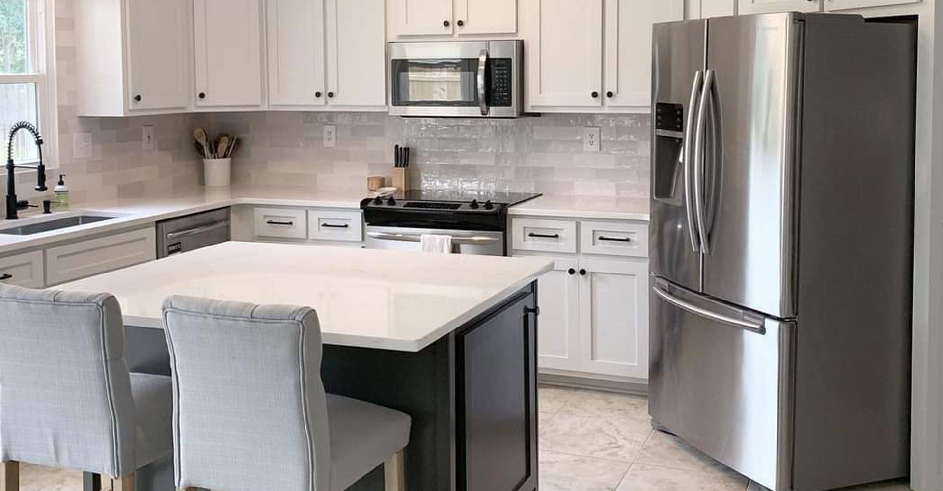 Modern kitchen with white cabinets, stainless steel appliances, island with two chairs, and gray tile backsplash.