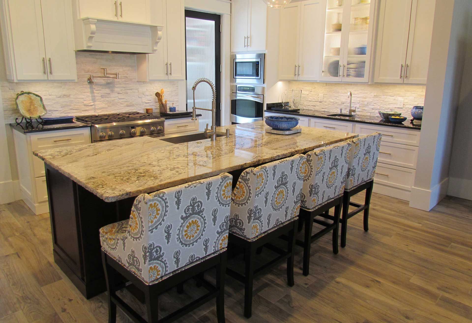 Kitchen with island, granite countertop, white cabinets, and patterned bar stools.