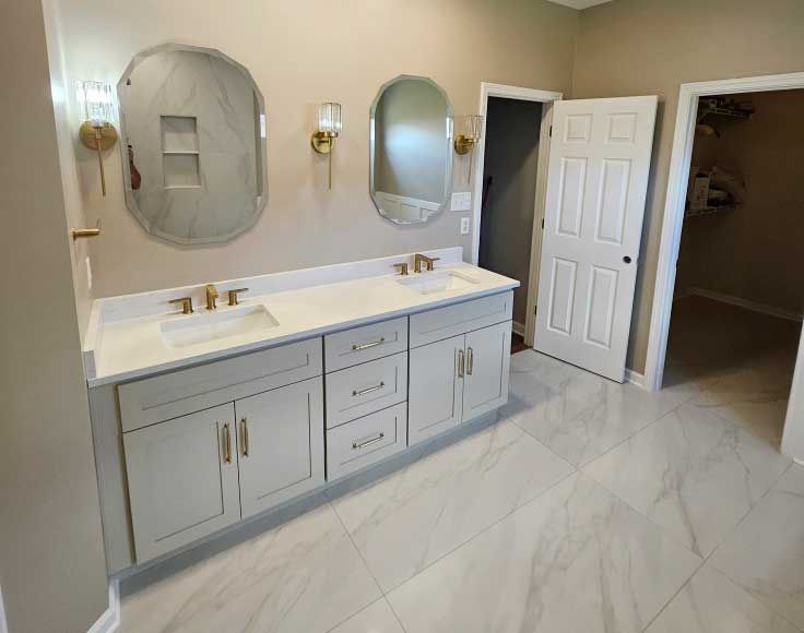 Bathroom with dual sinks, light gray cabinets, gold fixtures, and marble-look tile.