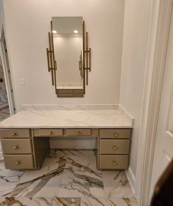 Vanity with marble countertop, gold drawers, mirror. Marble tile flooring. White walls.