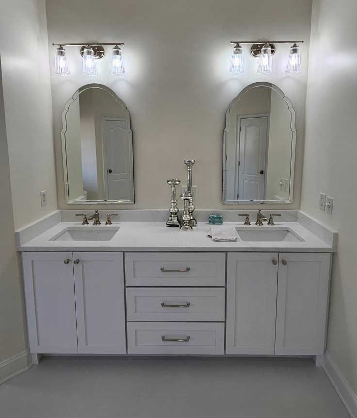 White double vanity with mirrors, lights, and décor in a light-colored bathroom.
