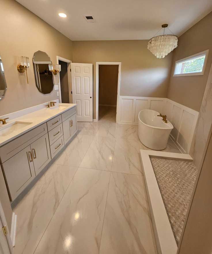 Spacious bathroom with marble floors, gray vanity, freestanding tub, and a chandelier.