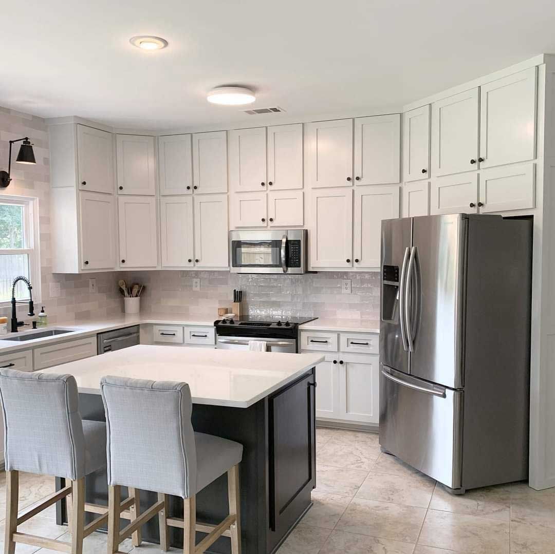 White kitchen with dark island, stainless steel appliances, and three bar stools.