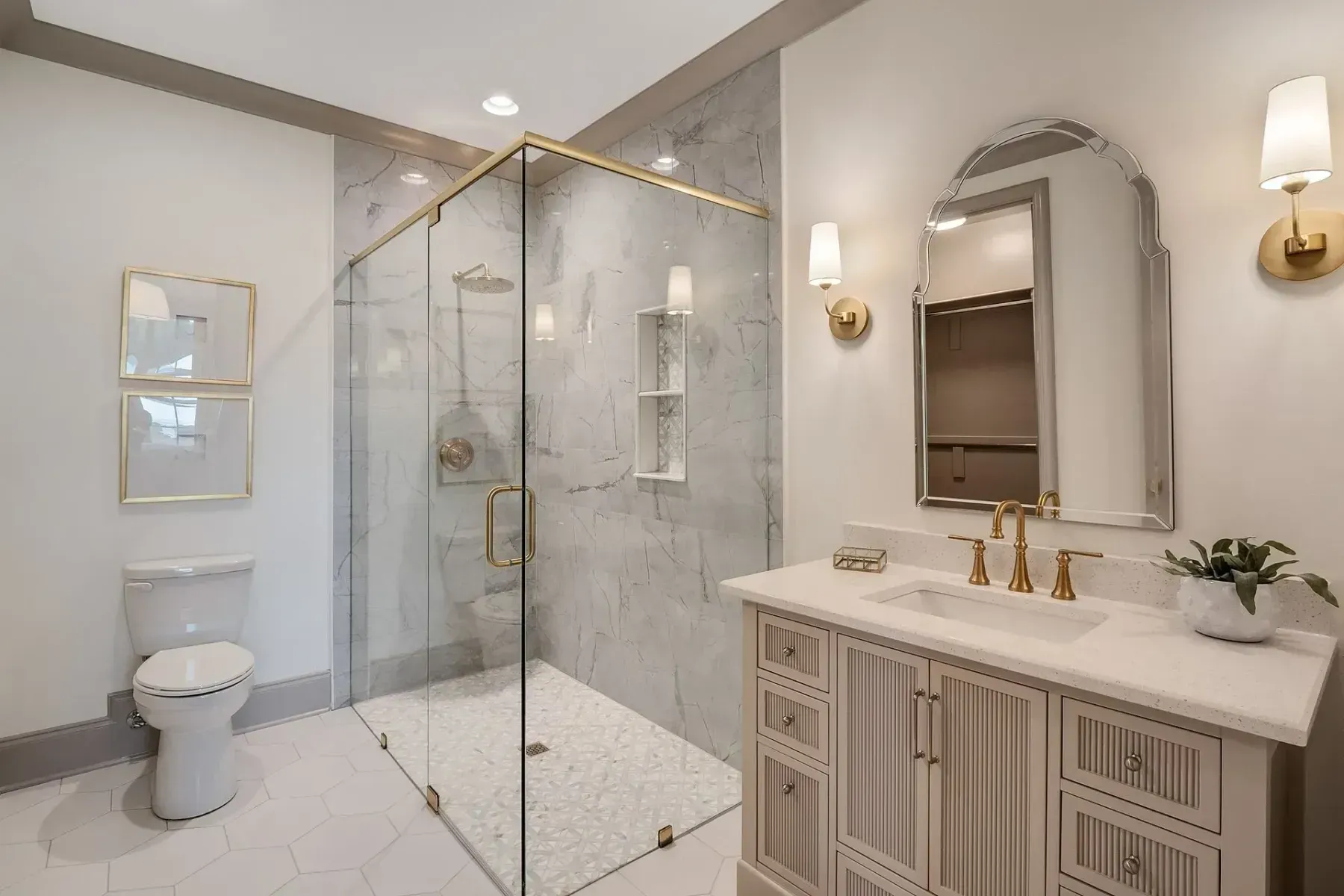Elegant white bathroom with glass shower, marble accents, gold fixtures, and a vanity.