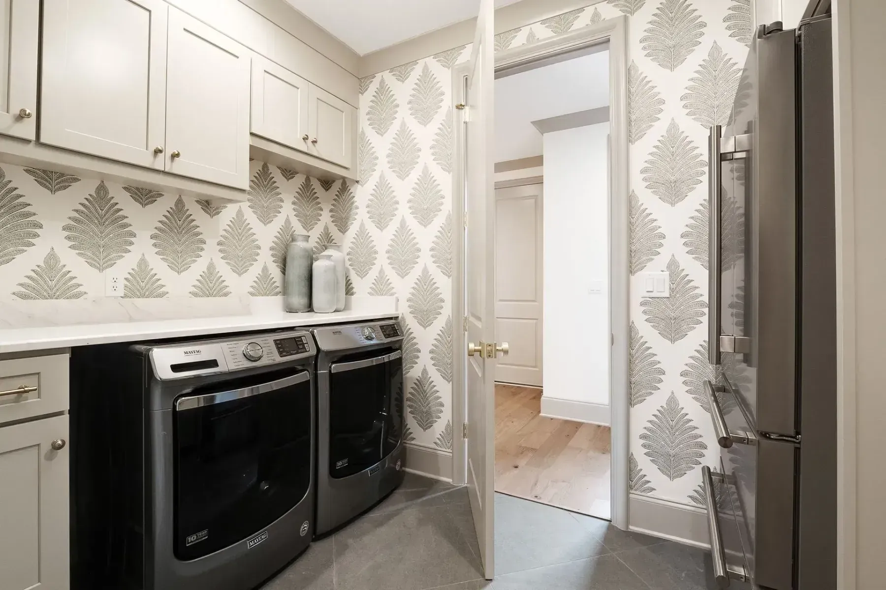 Laundry room with black washer/dryer, gray cabinets, and patterned wallpaper.
